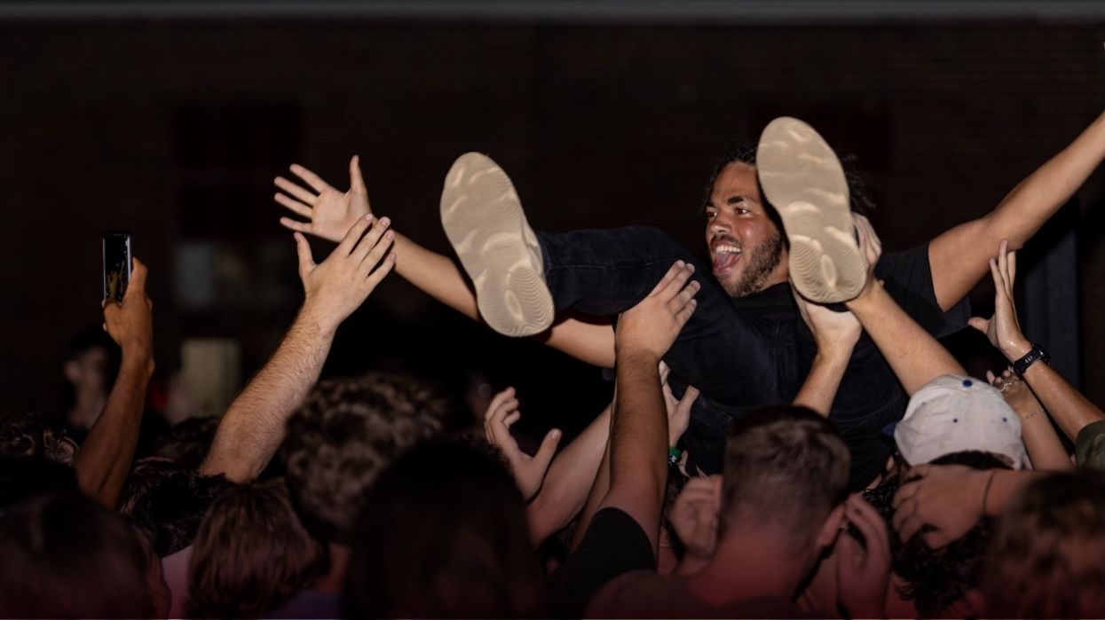A person with long hair is crowd surfing at a concert or event, supported by many hands in a cheering crowd. The scene is energetic and lively, with people reaching up and taking photos.