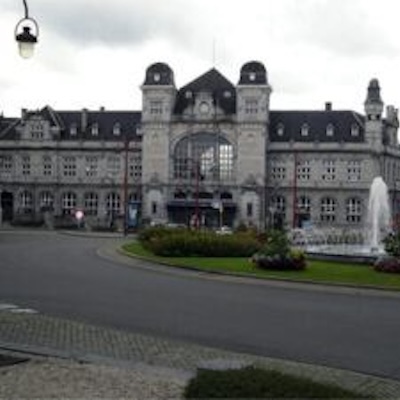 Large historic building in Belgium with stately facade and fountain, glimpsed from a road and green courtyard.