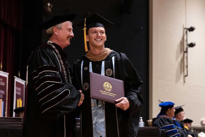 A student on stage with President Shannon during graduation