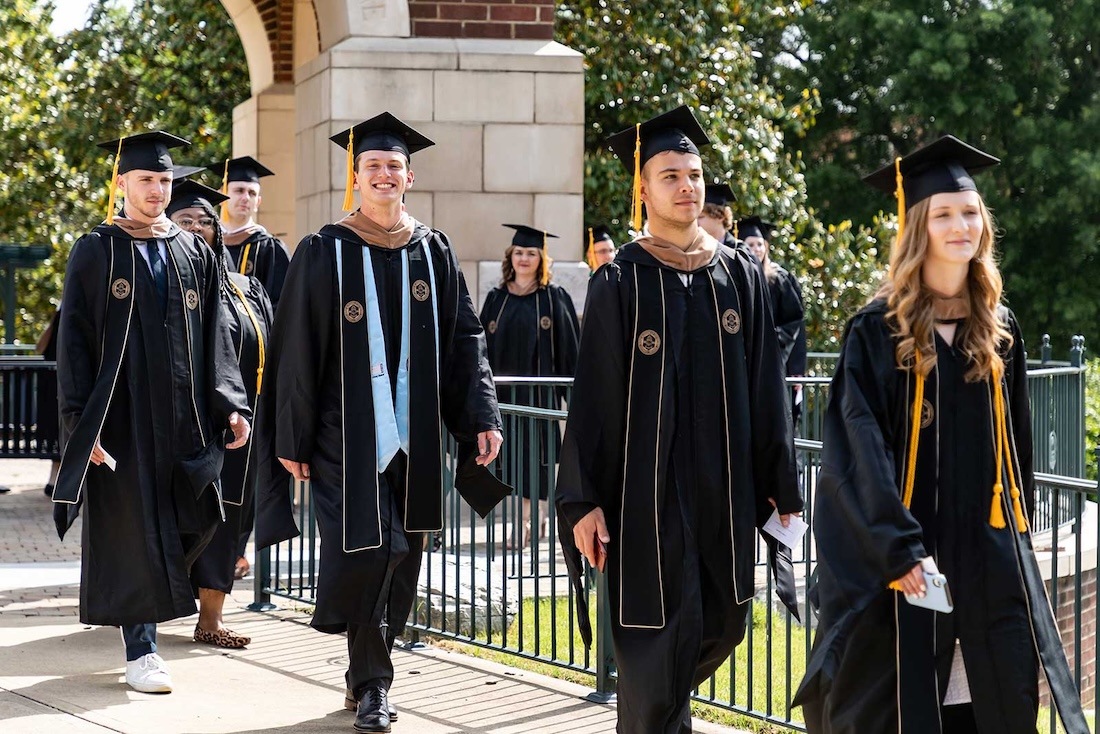 FHU graduates walking underneath the bell tower in the commons