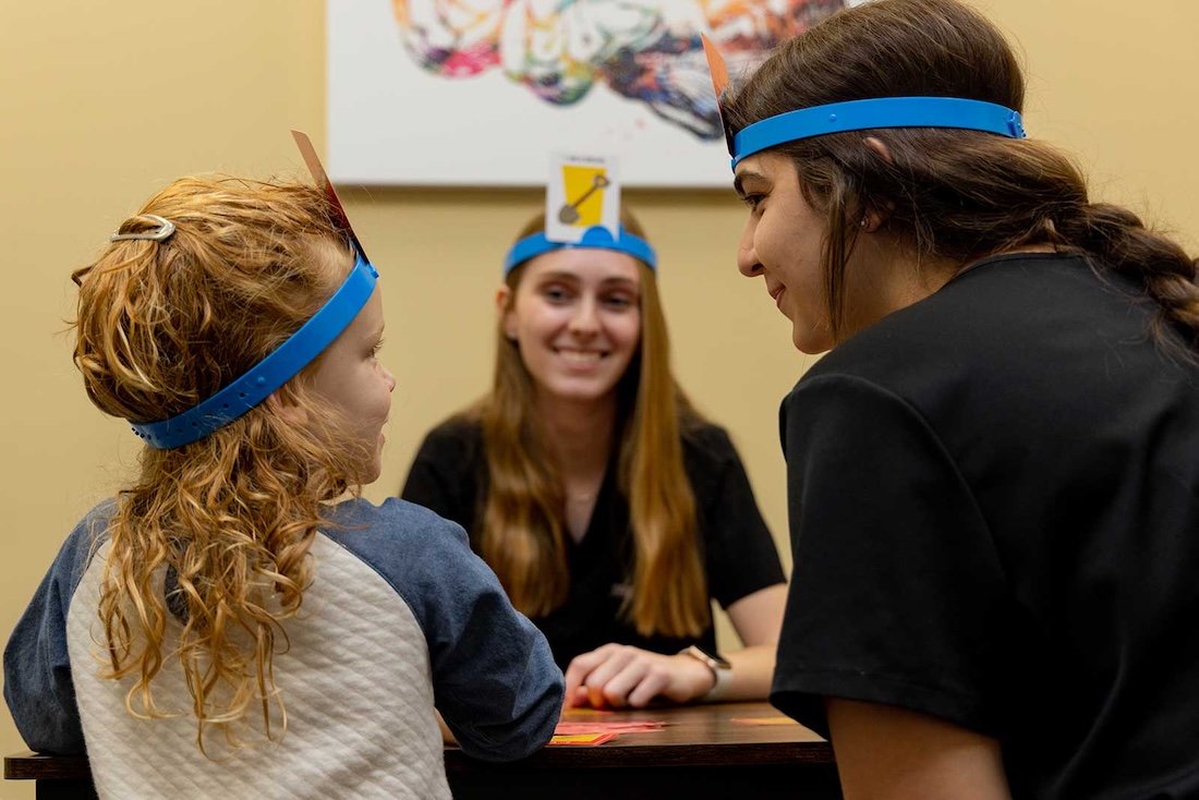 Two students playing a game with a child to promote a healthy learning environment