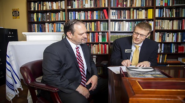 Justin Rogers talking to another man at his desk in his office