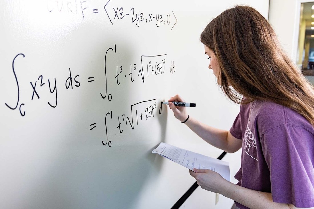 A student solves a complex math problem on a white board