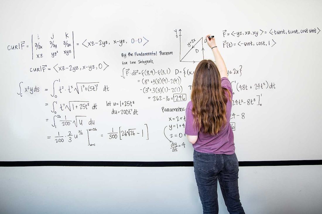 A student solves a complex math problem on a whiteboard in one of the library's study rooms