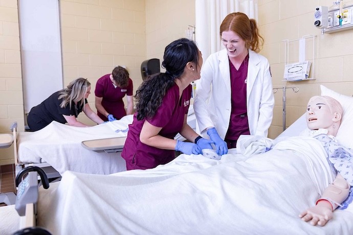 Two nursing students laughing with a nursing mannequin