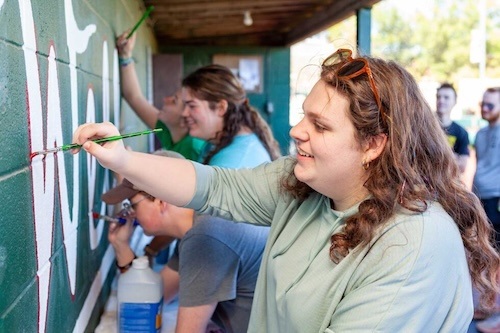 Students help paint the dugout wall at the baseball field