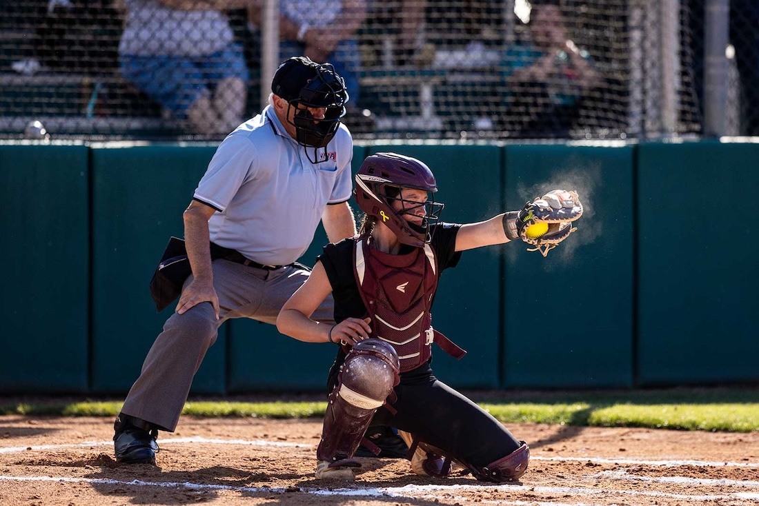 A softball catcher receives the pitch from the pitcher