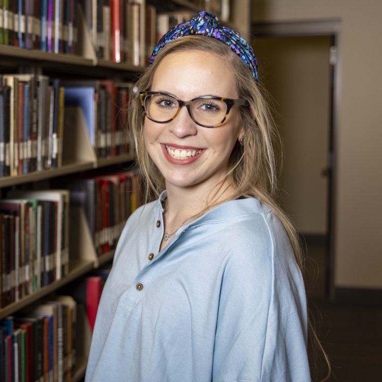 A student poses in front of one of the library shelves